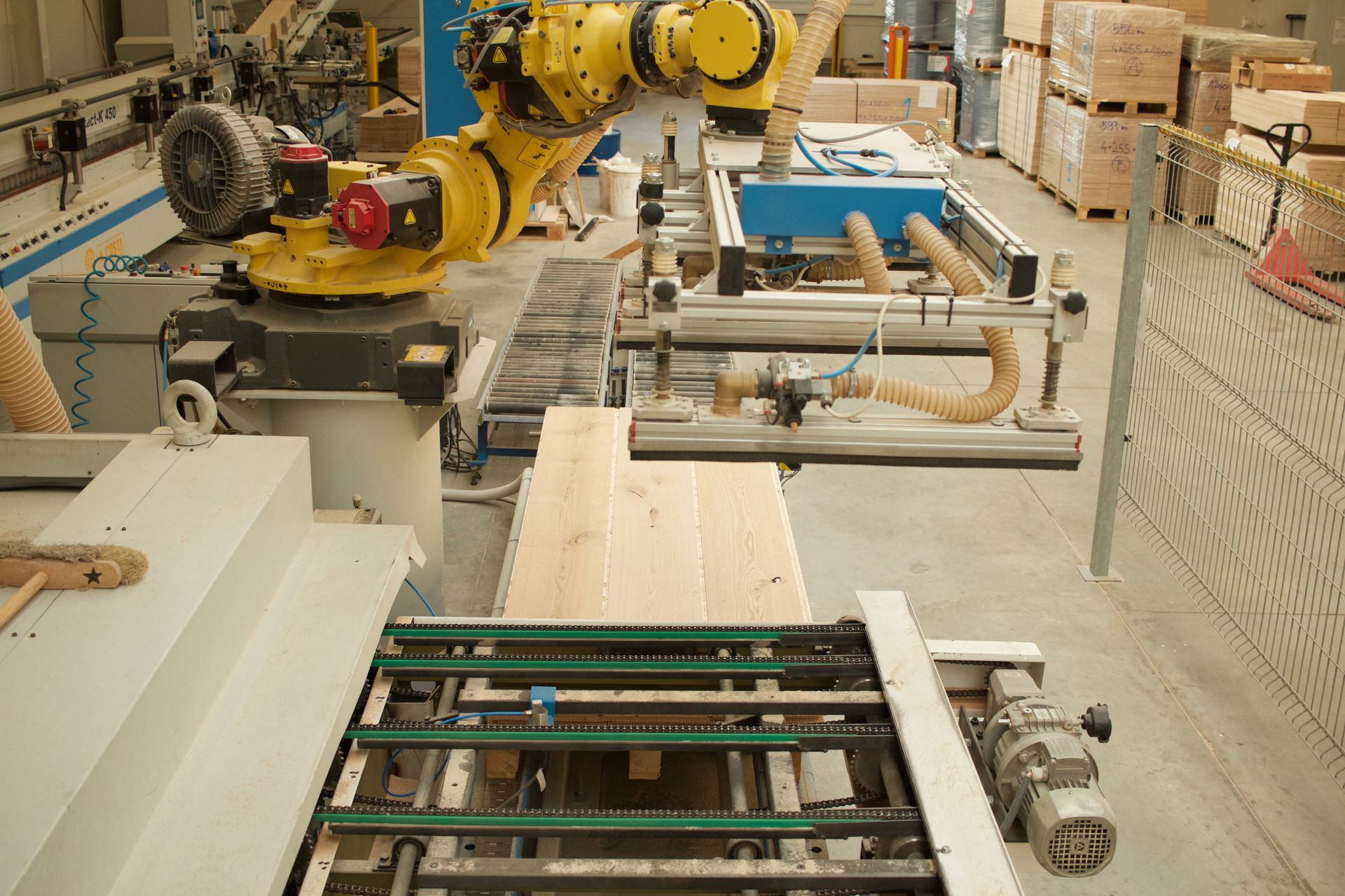 Pohled na automatizované pracoviště s průmyslovým robotem , který pomocí vakuových přísavek přesně manipuluje s rozměrnými dřevěnými deskami na výrobní lince.