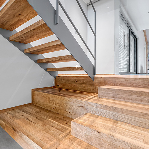 Moderní realizace levitujícího dubového schodiště Planet Parket v bílém interiéru s kovovým zábradlím a přirozeným osvětlením.