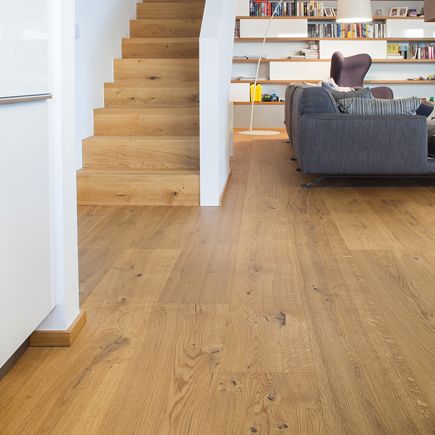 Detailní realizace dubové podlahy Planet Parket plynule navazující na dřevěné schodiště v moderním interiéru obývacího pokoje.